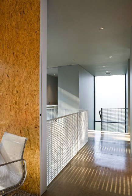  House on Lake Okoboji: View of hallway looking towards stairs with steel grate railing, concrete floor and wood panels. Rougher materials become sophisticated and elegant with detailing. Photo: Paul Crosby