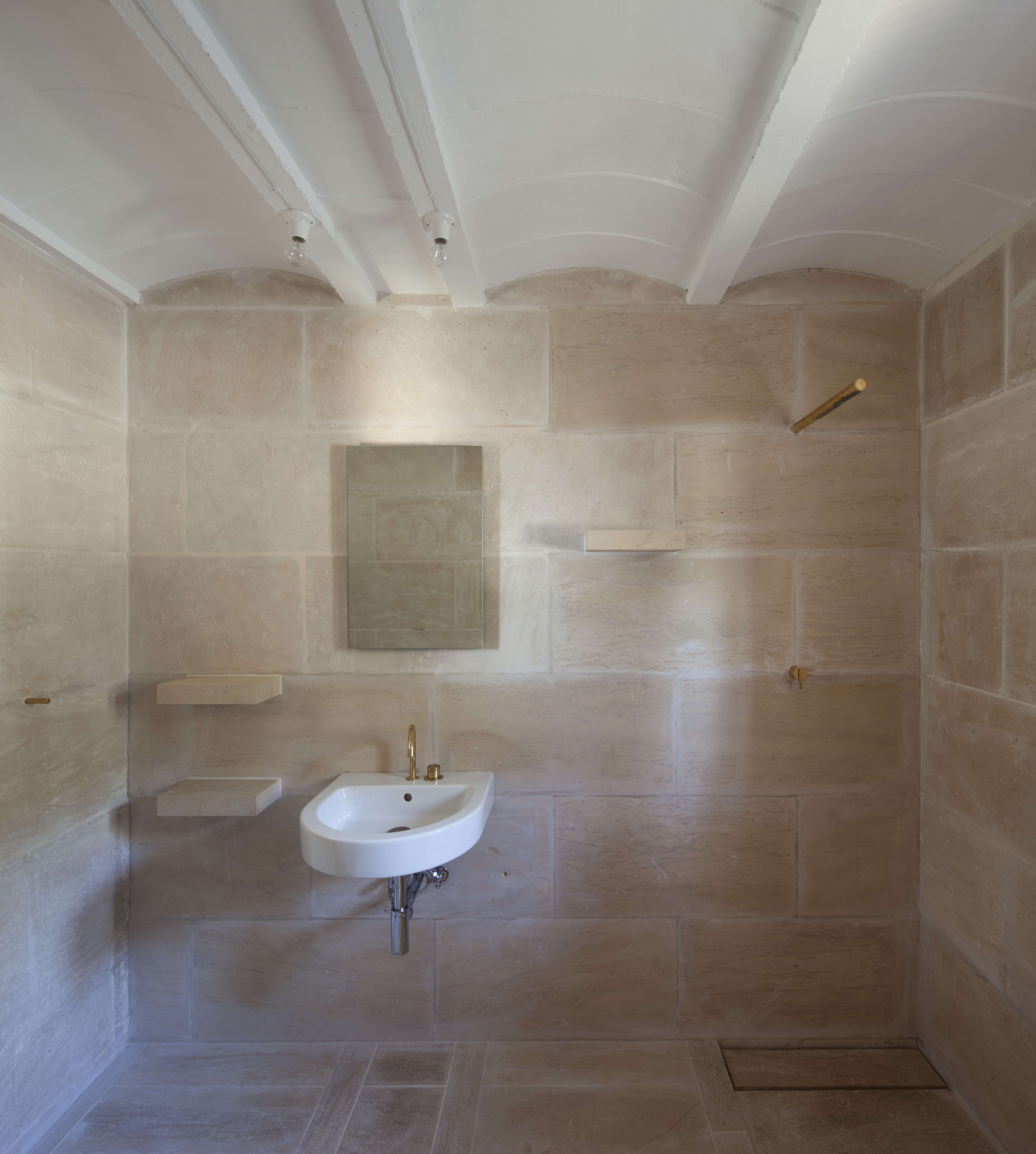 The bare bones bath features almost invisible shower fixtures and integrated stone shelving.