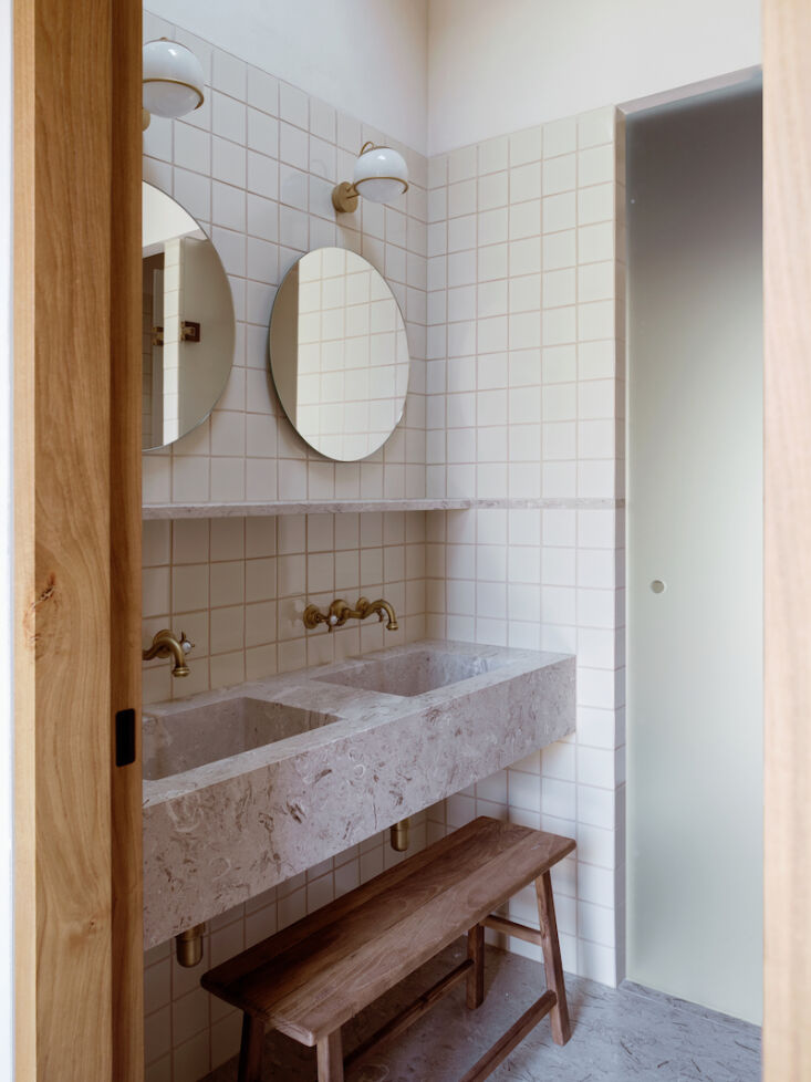 in the bathrooms, details include milk white tiles, circular mirrors, brass wal 27