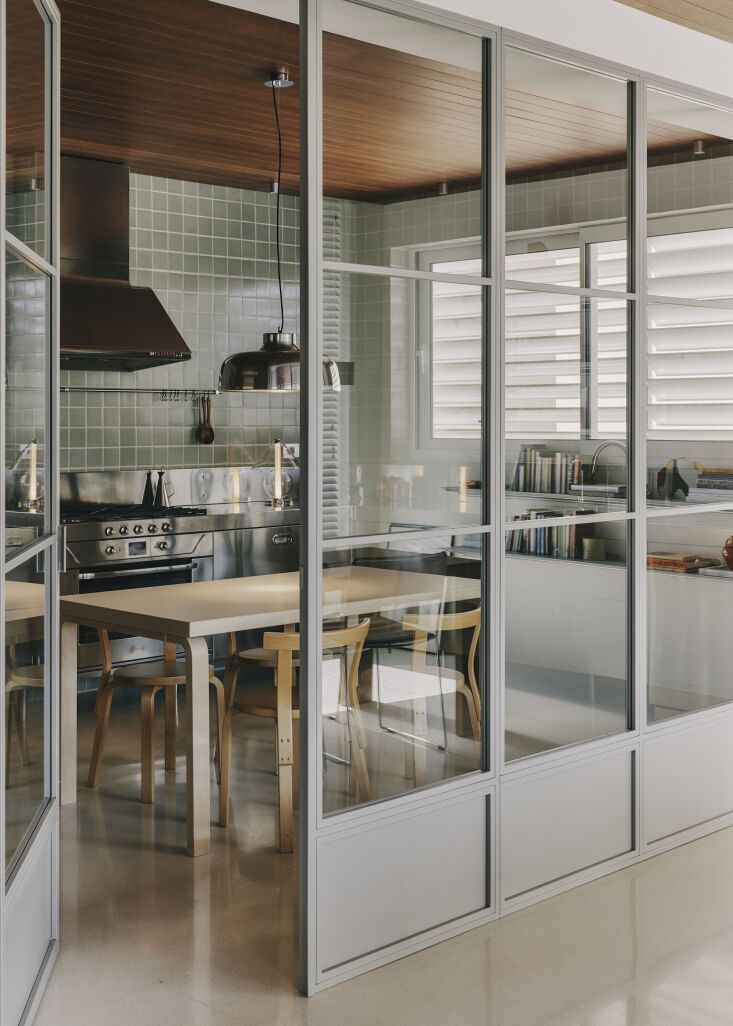 an eat in kitchen is enclosed by a steel and glass wall, a solution that allows 18