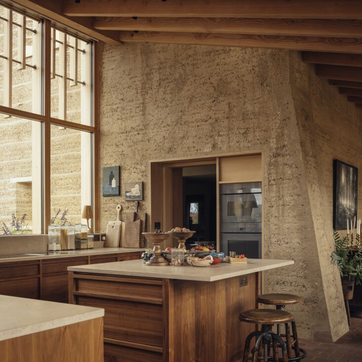 set among rammed earth and oak framing are two miele wall ovens. a custom islan 23