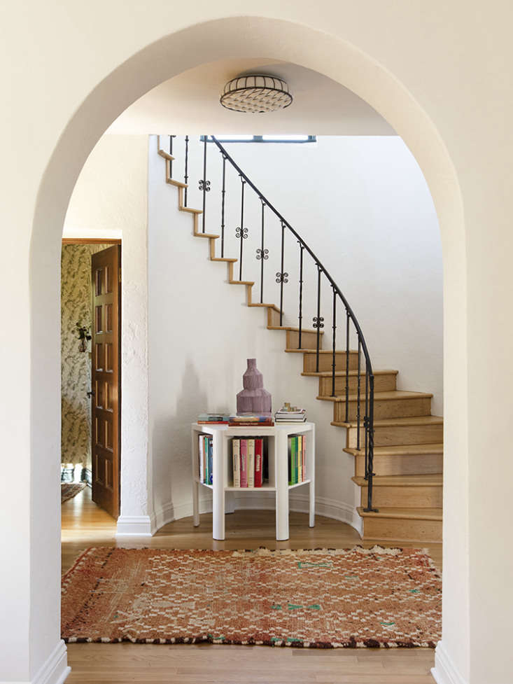 a martin & brocket library table stands in the entry under a curved stair.  10