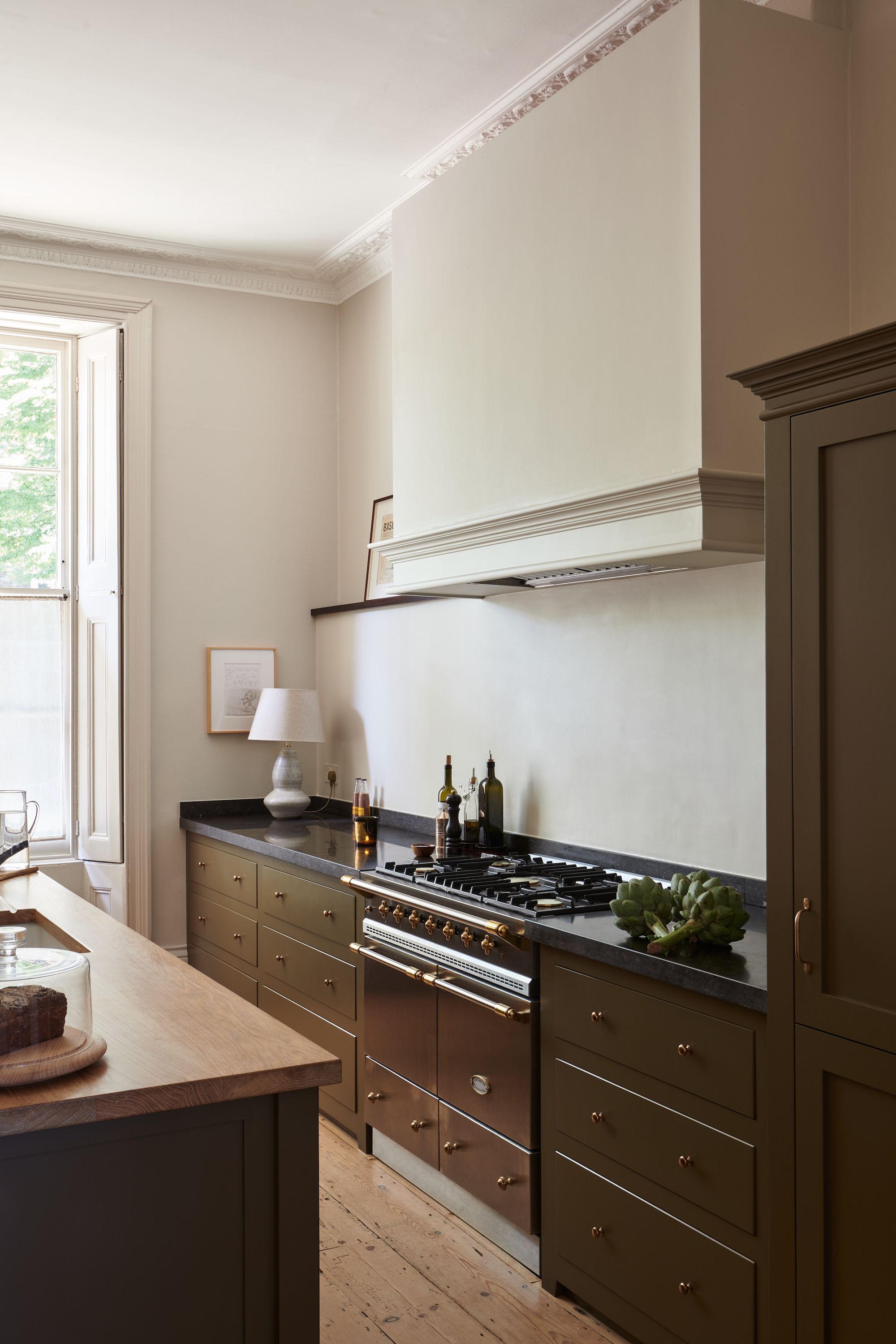 a black and brass french lacanche range is set into brown and brass cabinetry.  10