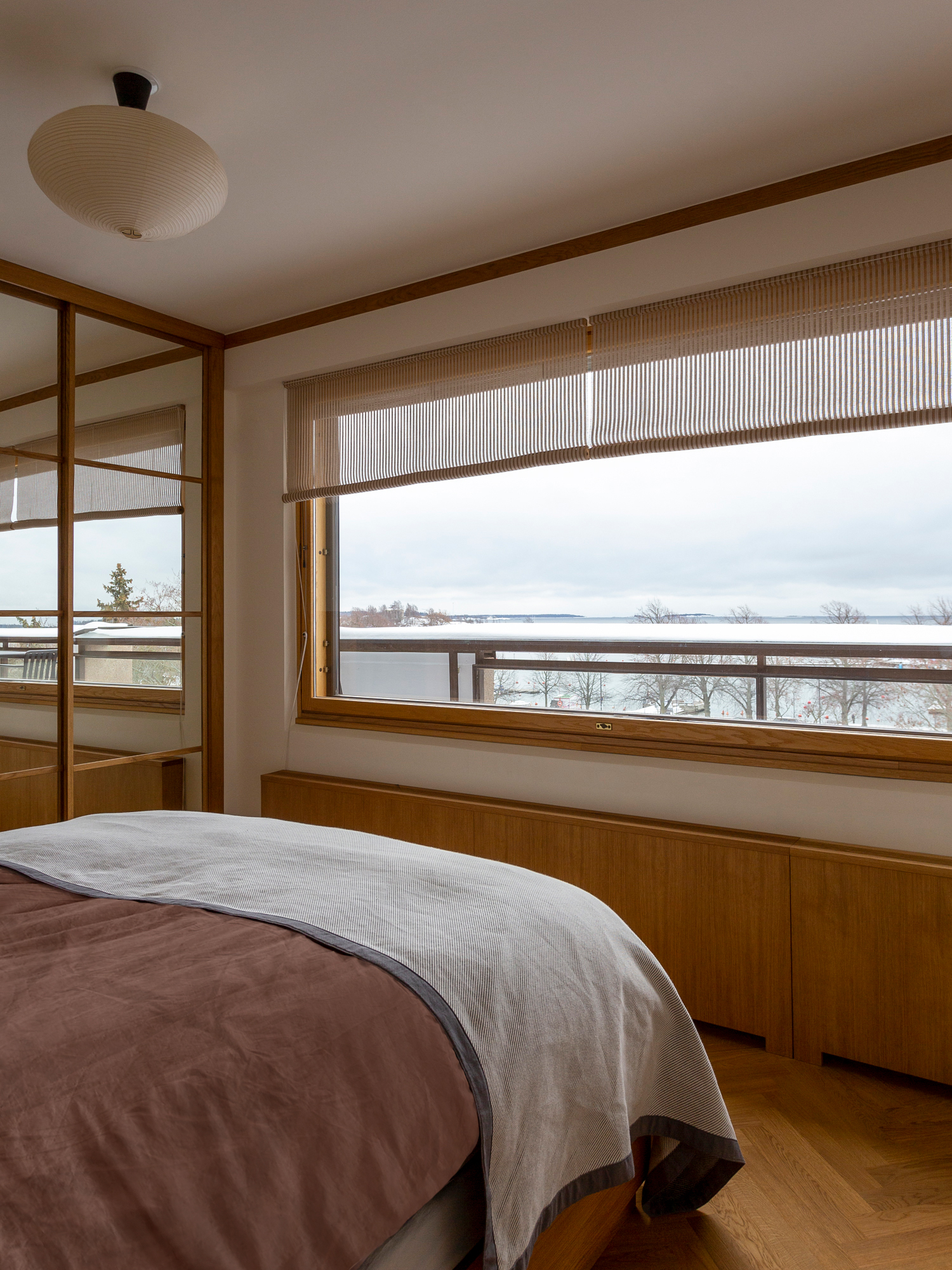 a bedroom with a window looking out onto the sea. the blinds are from woodnotes 17