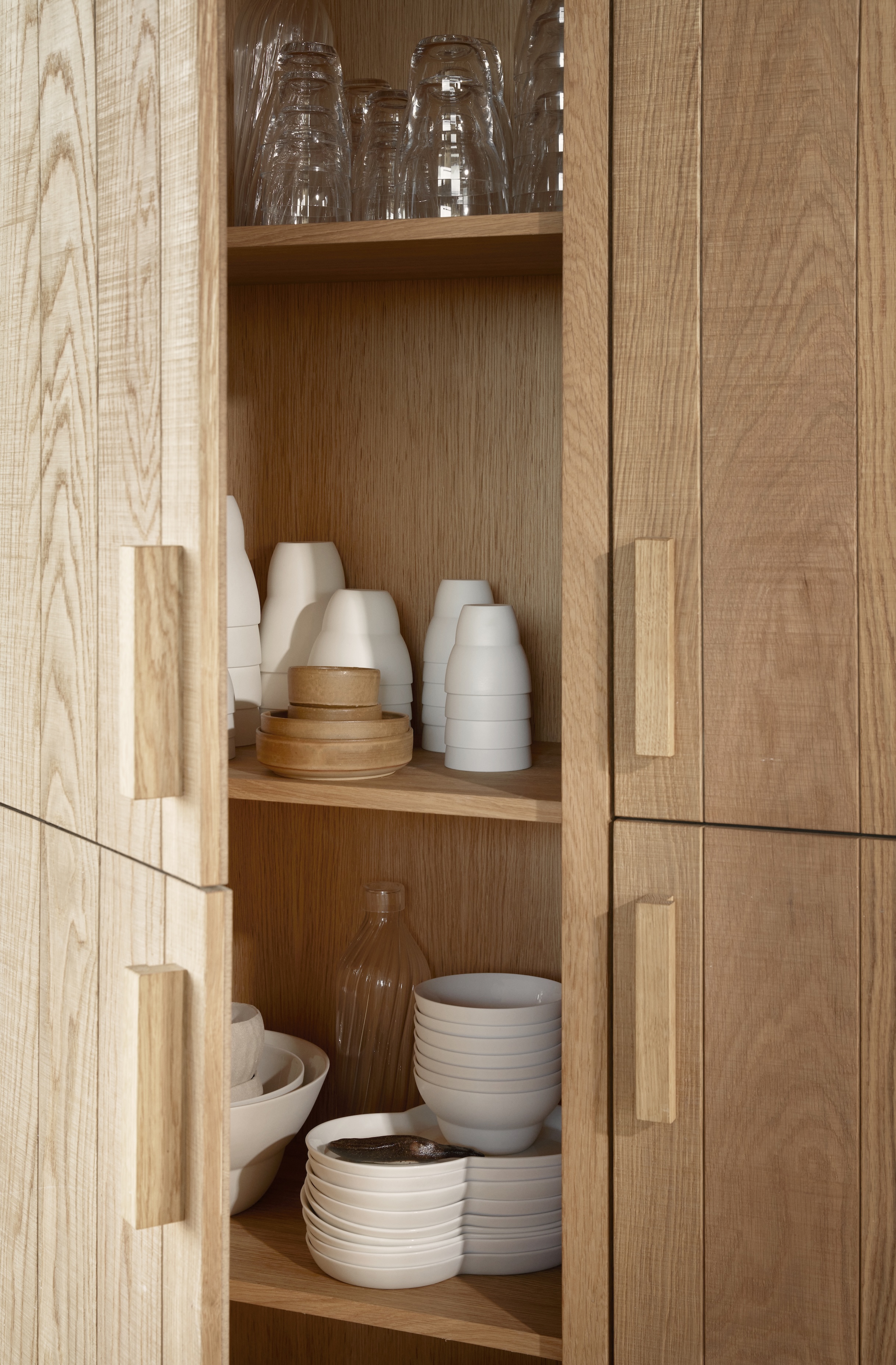 a built in oak cabinet holds vipp tea and coffee cups, plates, bowls, and other 22